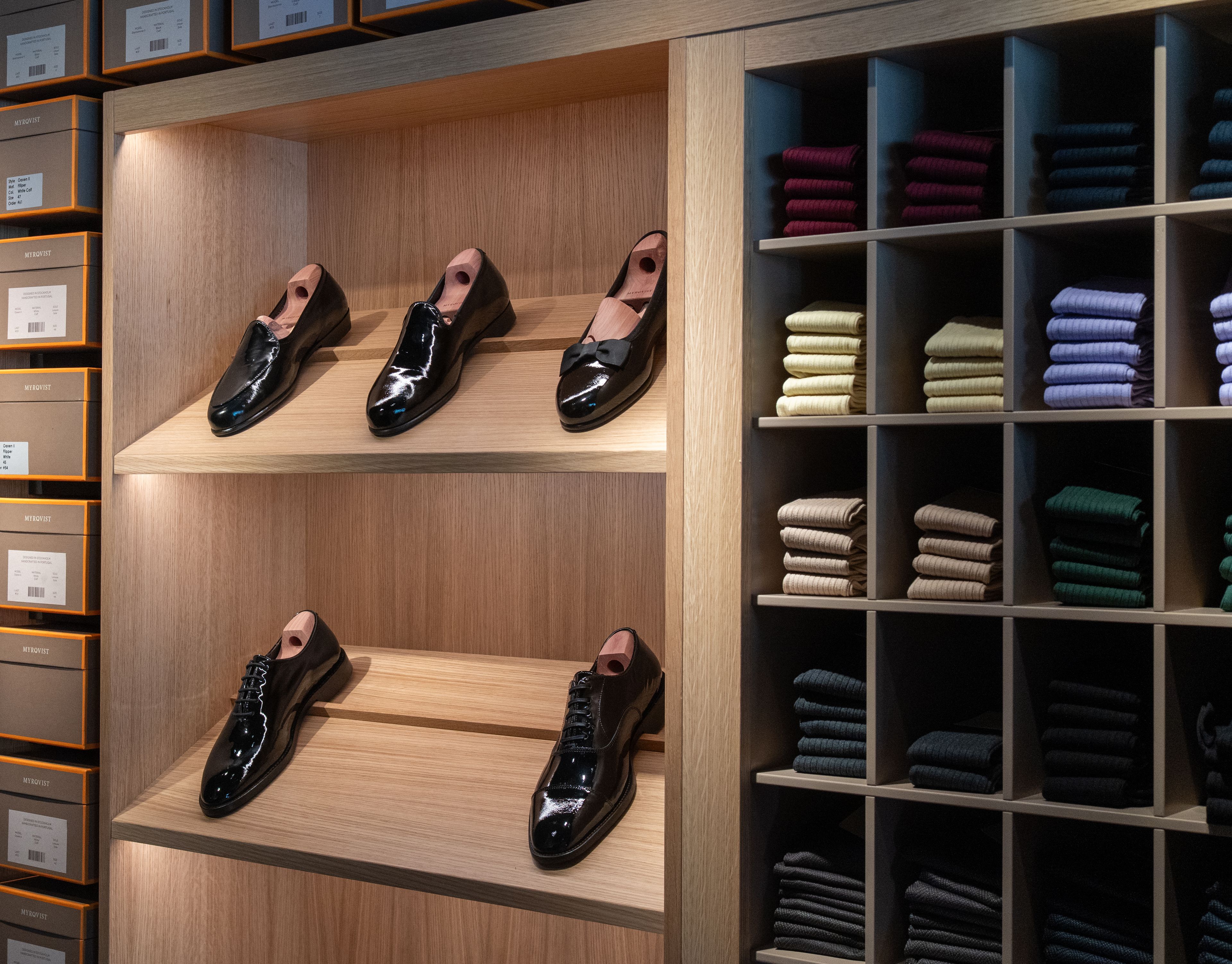 Patent leather shoes on wooden shelves next to colorful folded socks in cubbies.