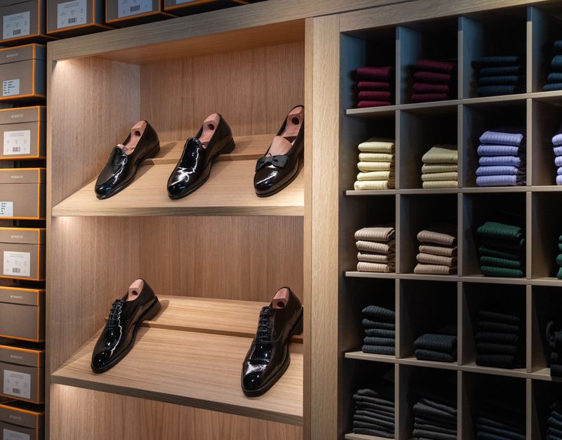Patent leather shoes on wooden shelves next to colorful folded socks in cubbies.