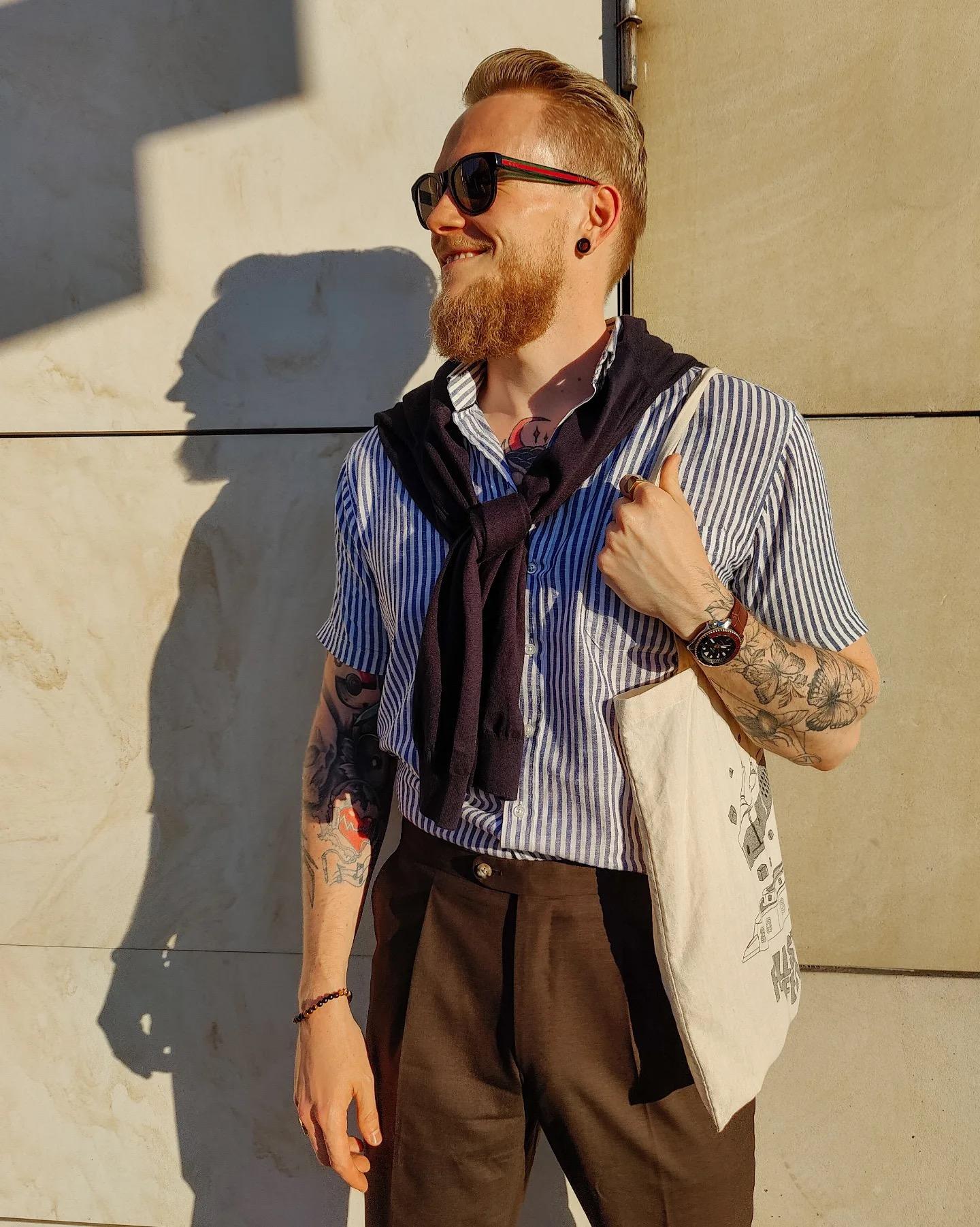 a man with a beard is wearing a striped shirt and brown pants