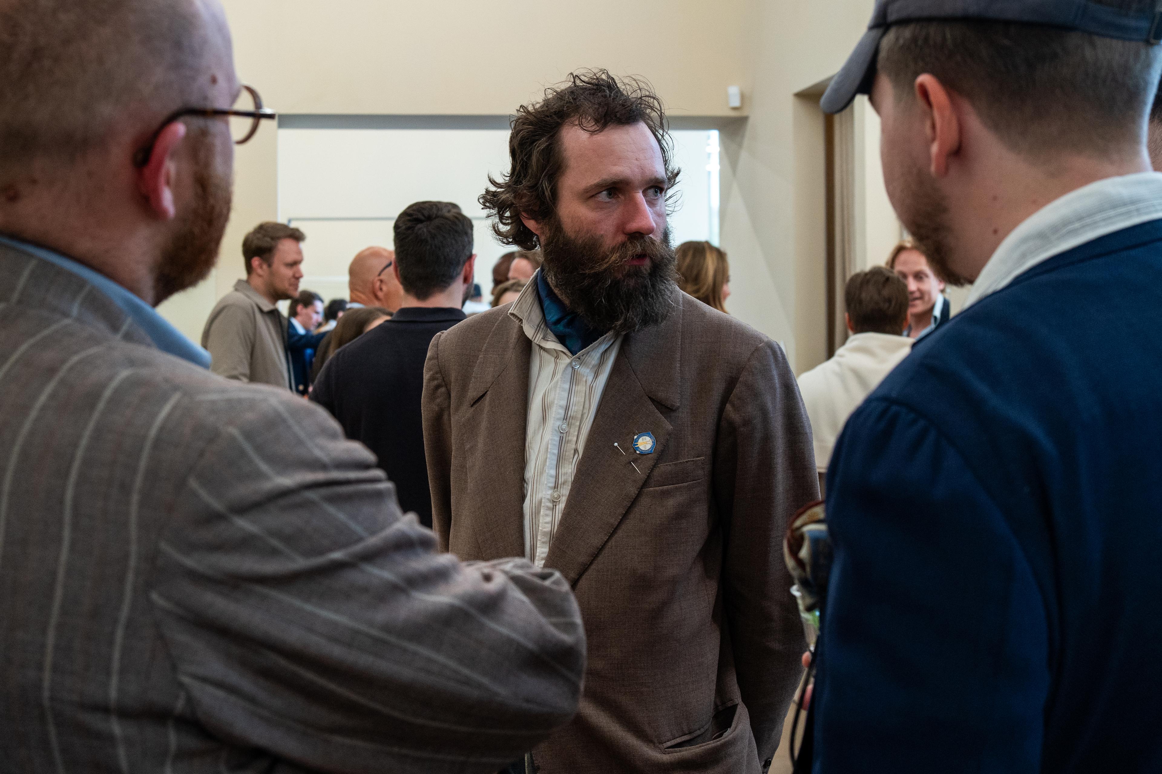 a man with a beard is talking to two other men in a room .
