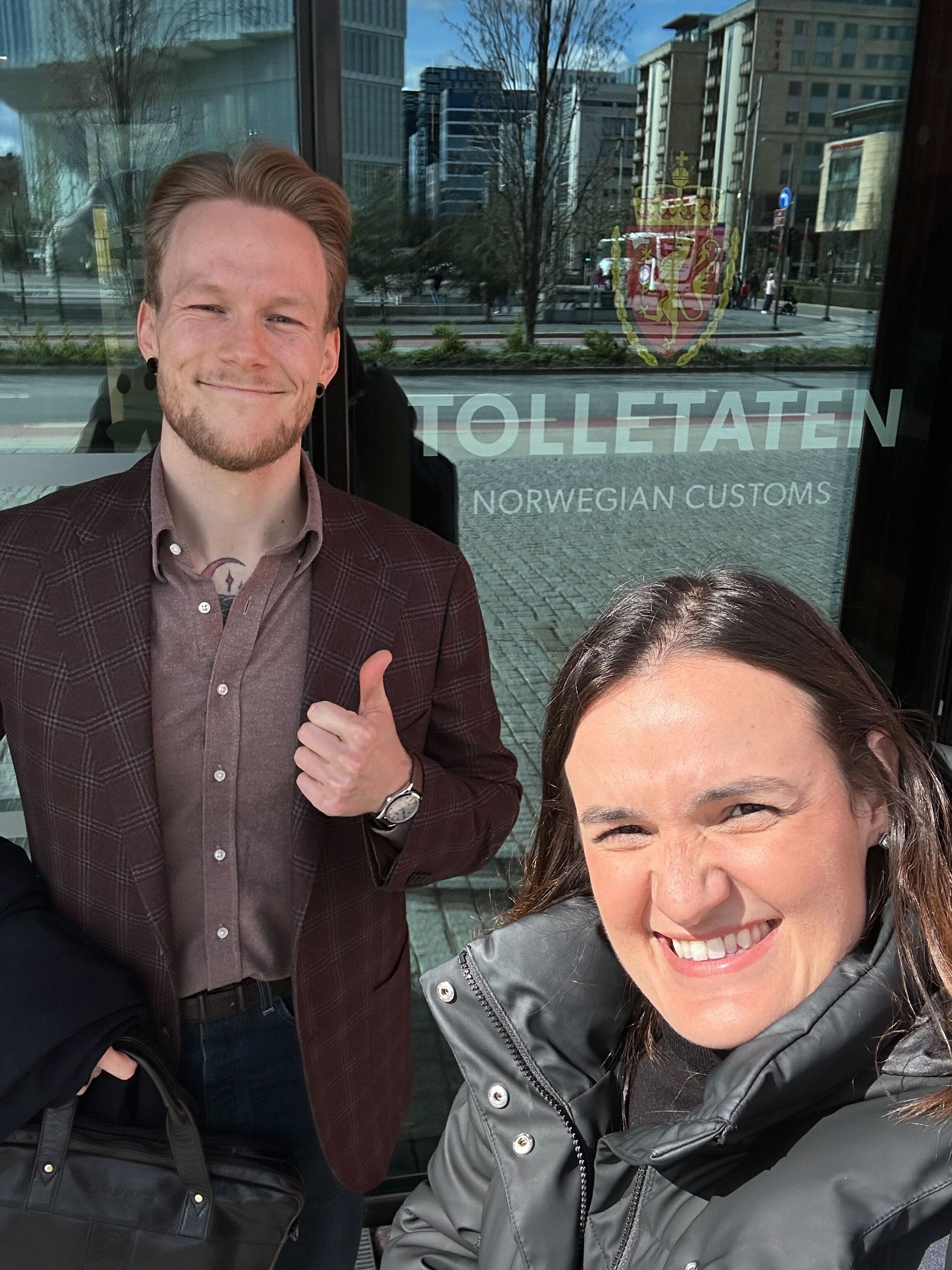 a man and a woman are standing in front of a sign that says tolletaten norwegian customs