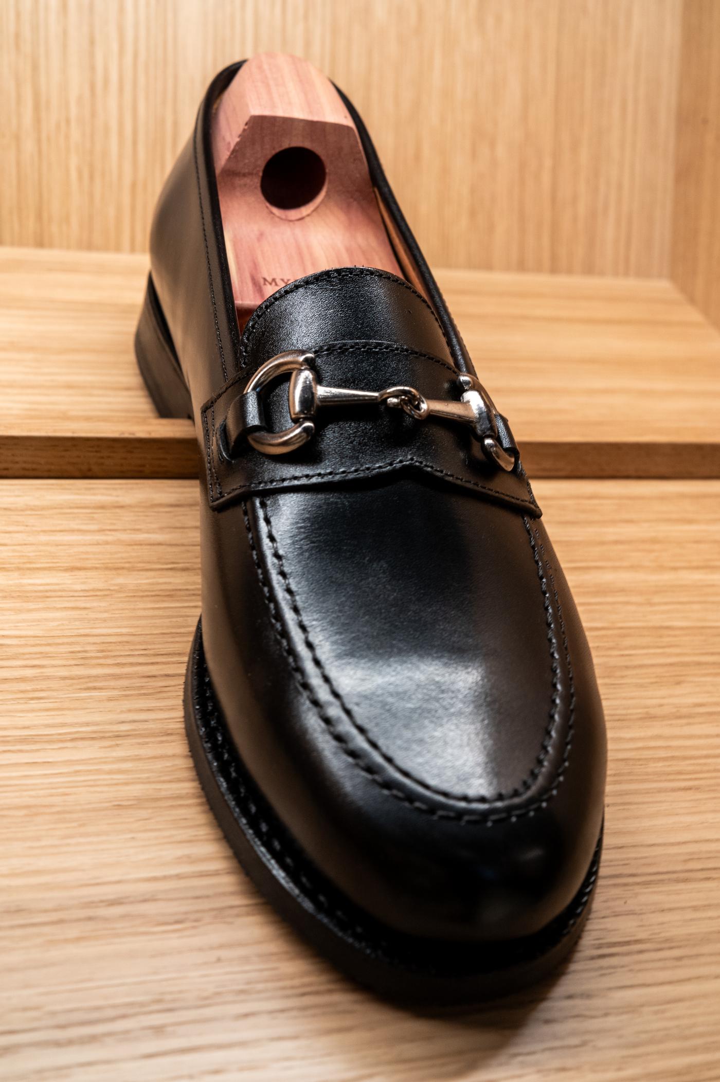 a pair of black loafers sitting on a wooden shelf