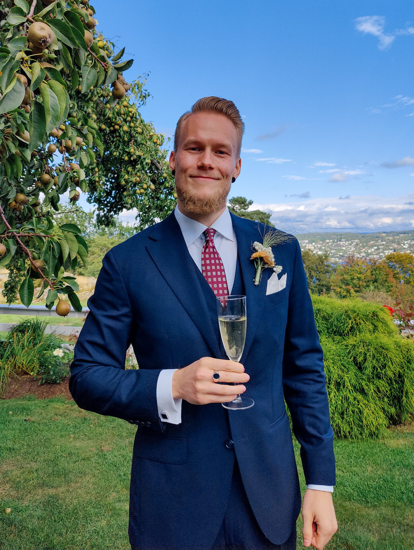 Kristoffer wearing a navy suit, holding a glass of champagne in a picturesque garden