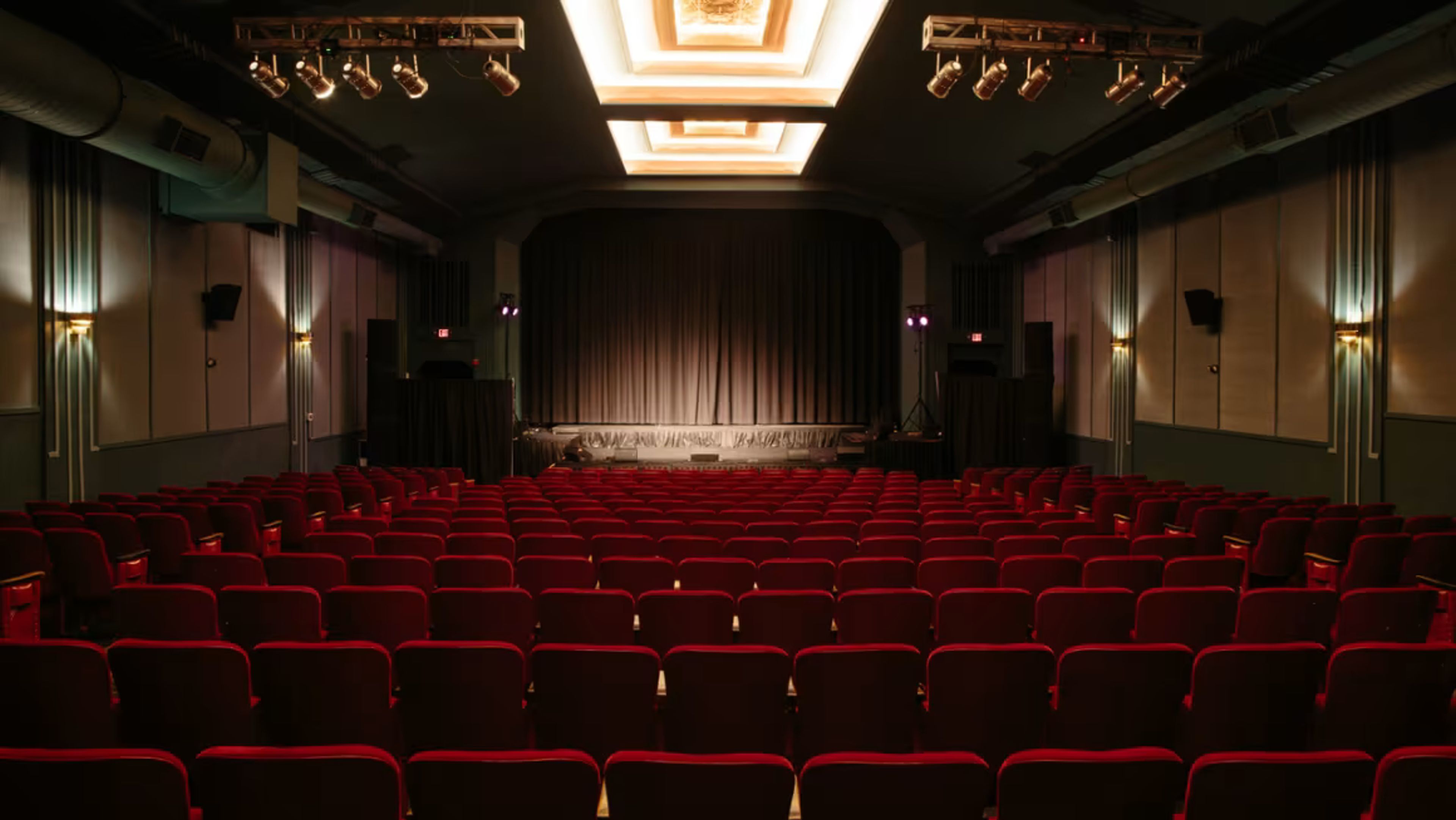 Rows of empty red seats face a stage with dark curtains in an intimate theater.