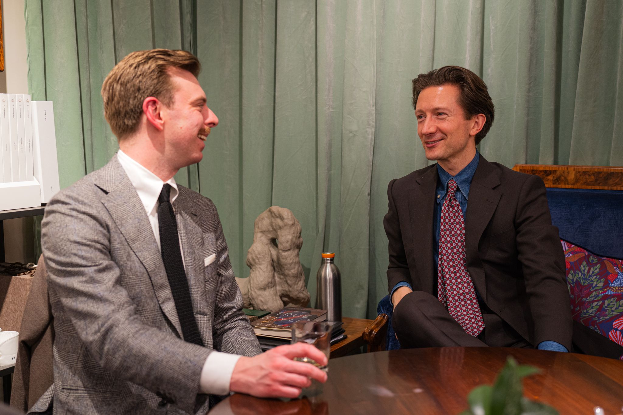 Two stylish men in pleasant conversation over a drink