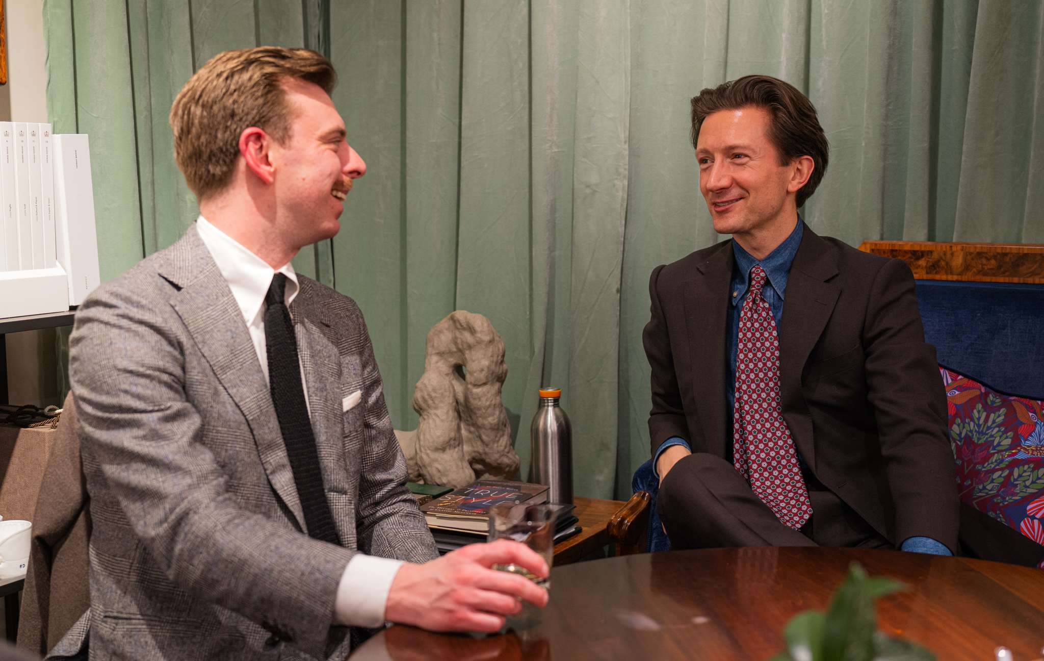 Two stylish men in pleasant conversation over a drink
