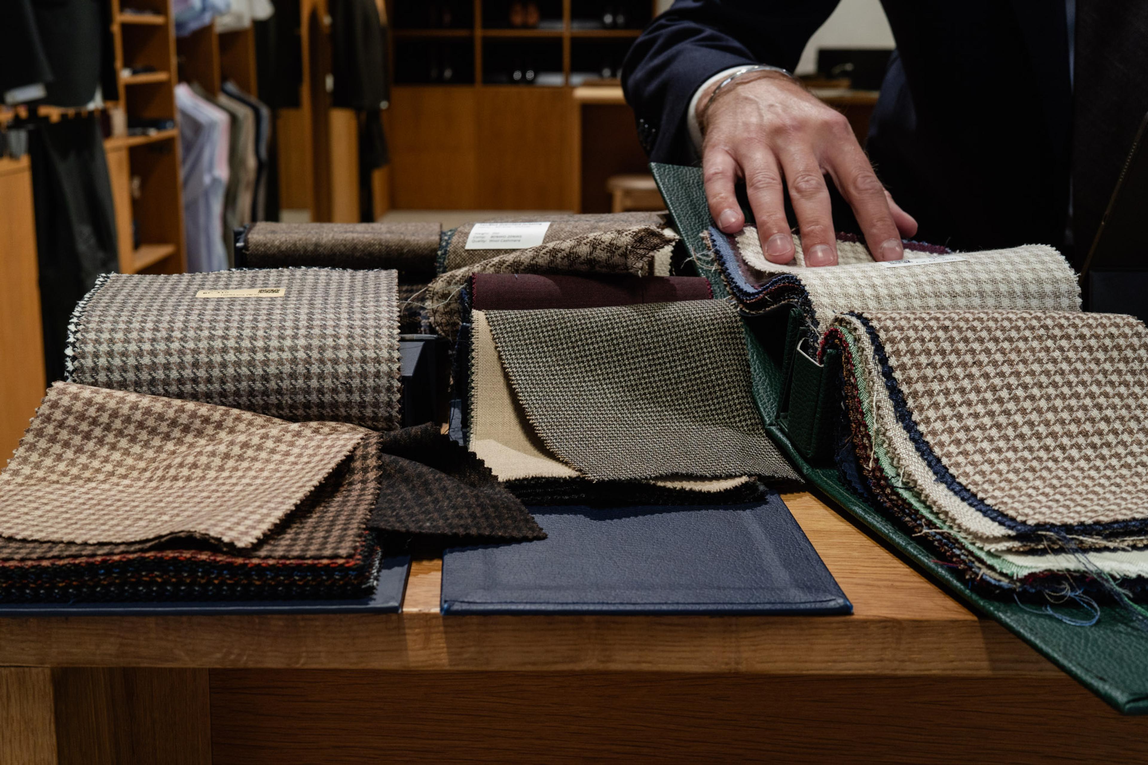 A hand selects from a variety of fabric swatches, including houndstooth patterns, on a wooden table.