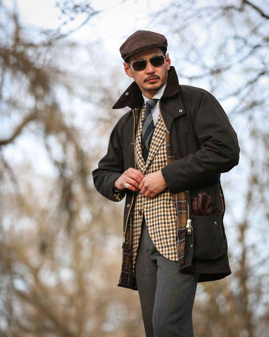 a man wearing a hat and sunglasses adjusts his jacket