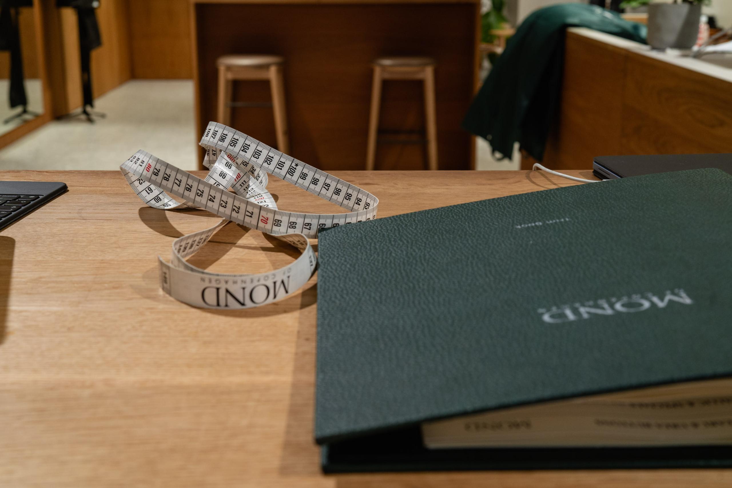 A coiled measuring tape and a dark green "MOND" binder on a wooden table.