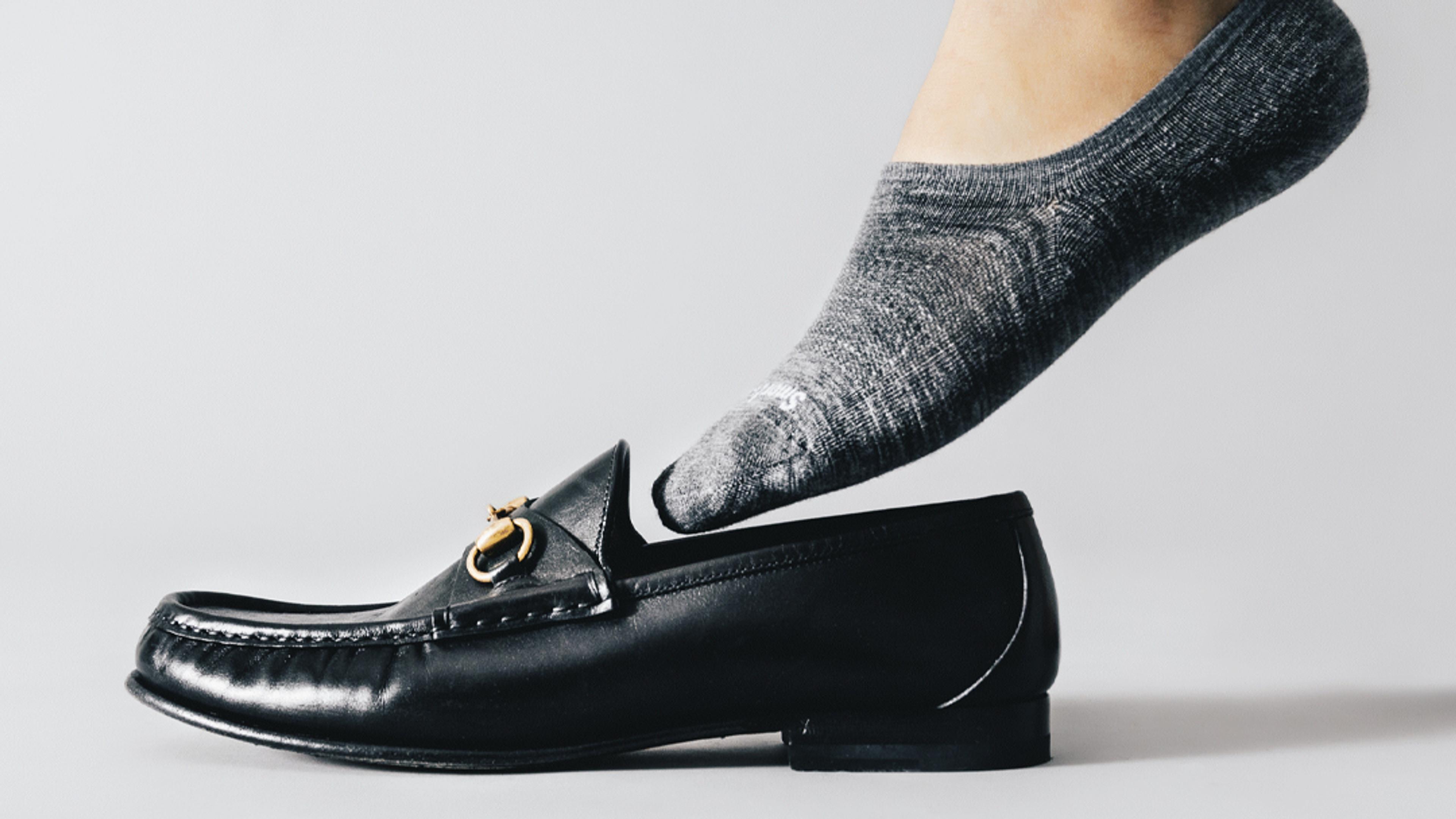 Foot in gray no-show sock preparing to enter black loafer.