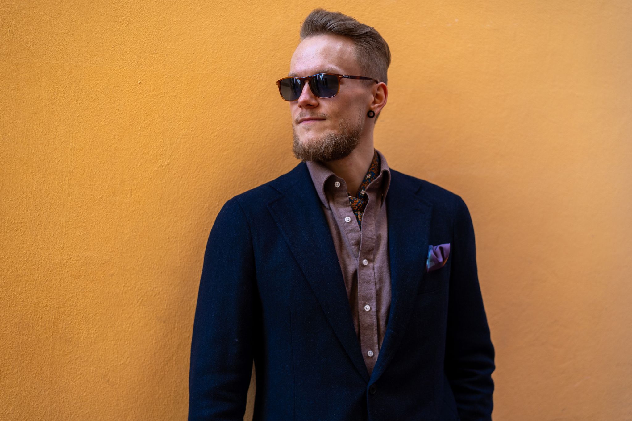 a man in a suit and sunglasses is standing in front of a yellow wall .