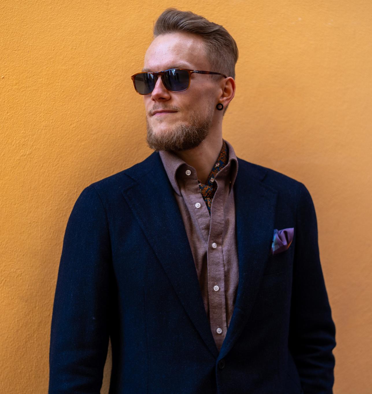a man in a suit and sunglasses is standing in front of a yellow wall .