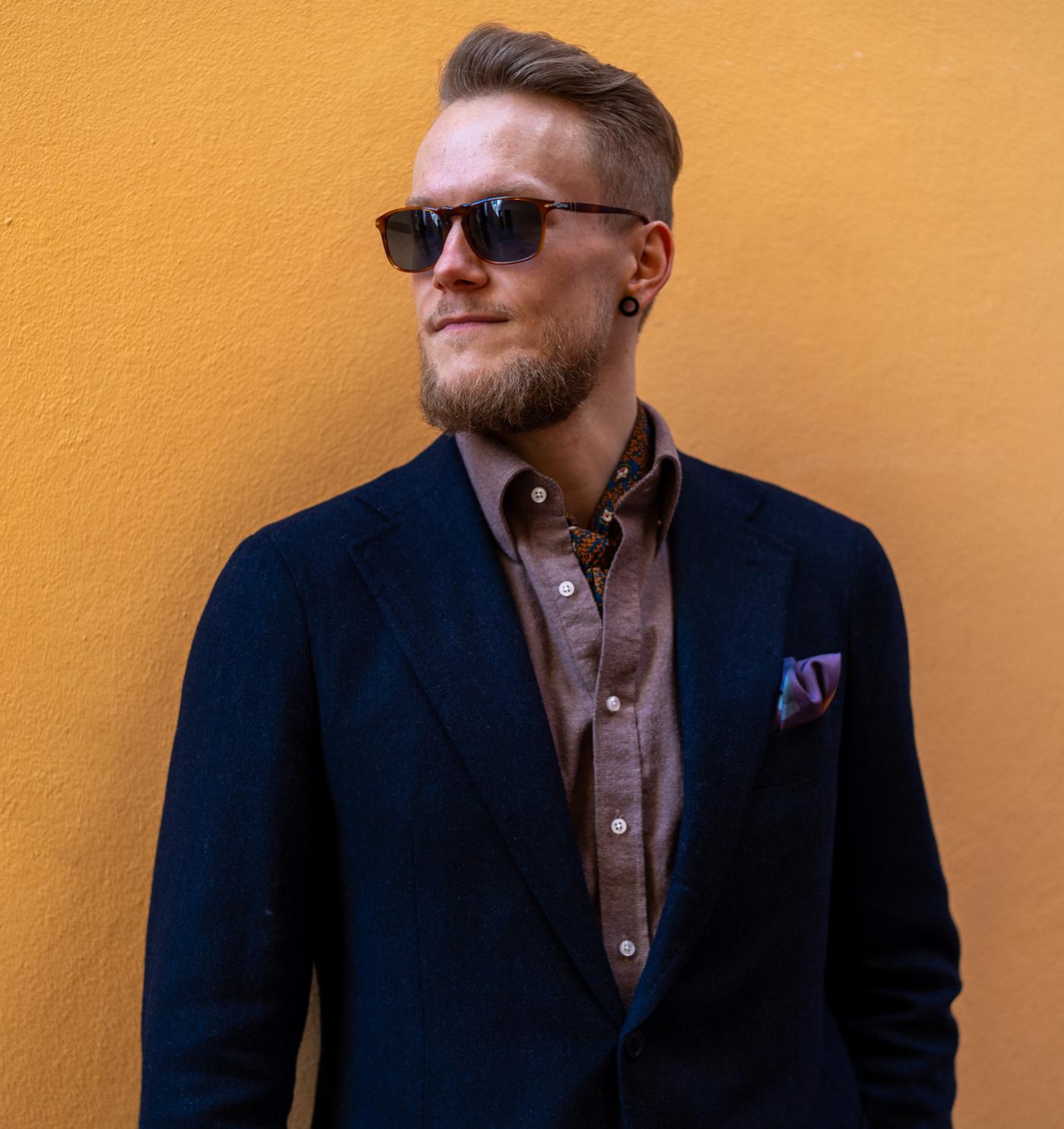 a man in a suit and sunglasses is standing in front of a yellow wall .