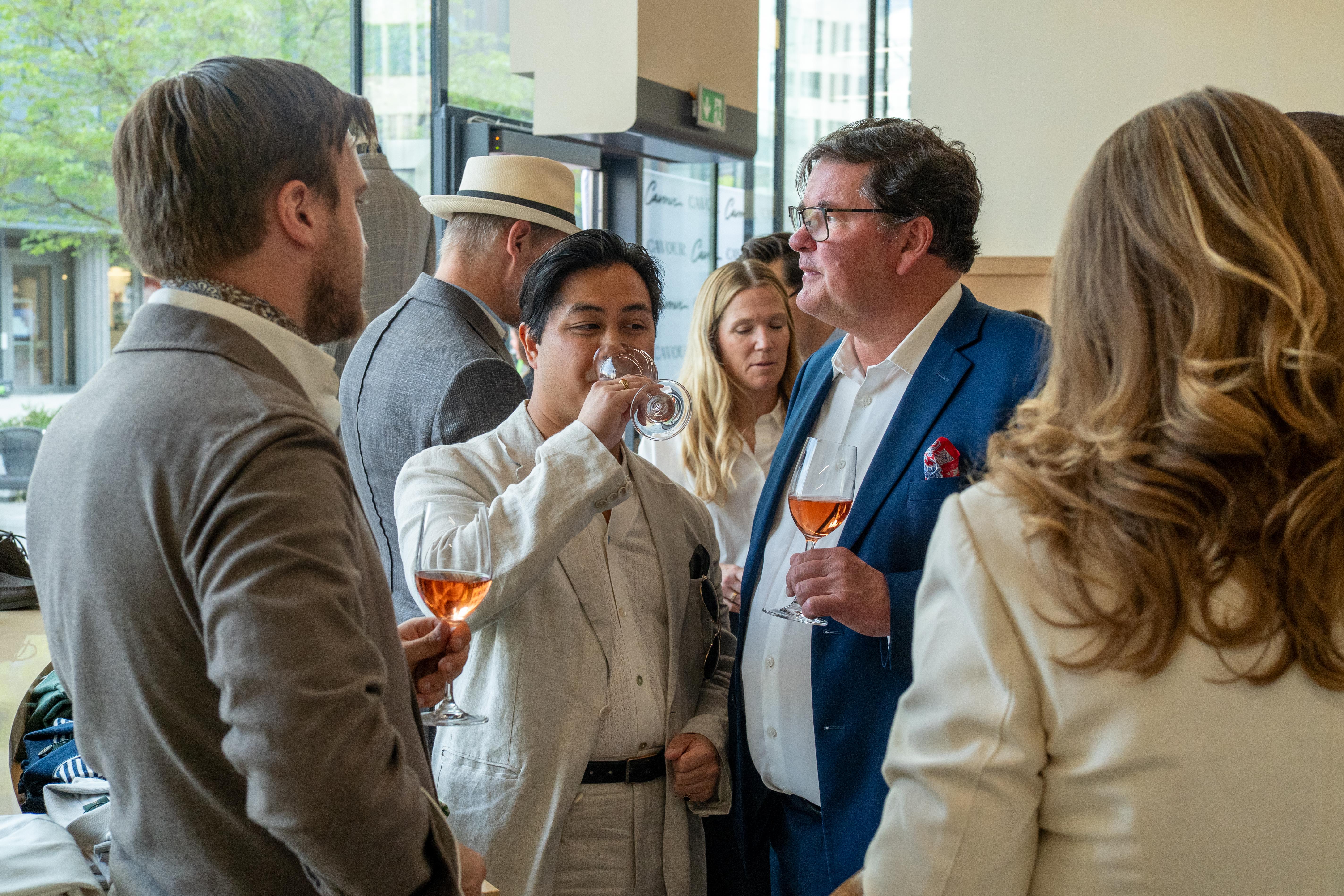 a group of people are standing around talking and drinking wine .