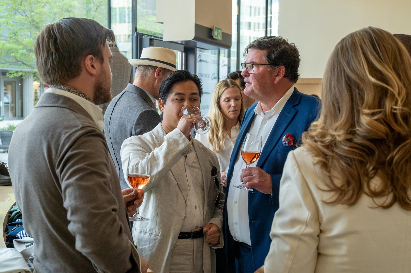 a group of people are standing around talking and drinking wine .