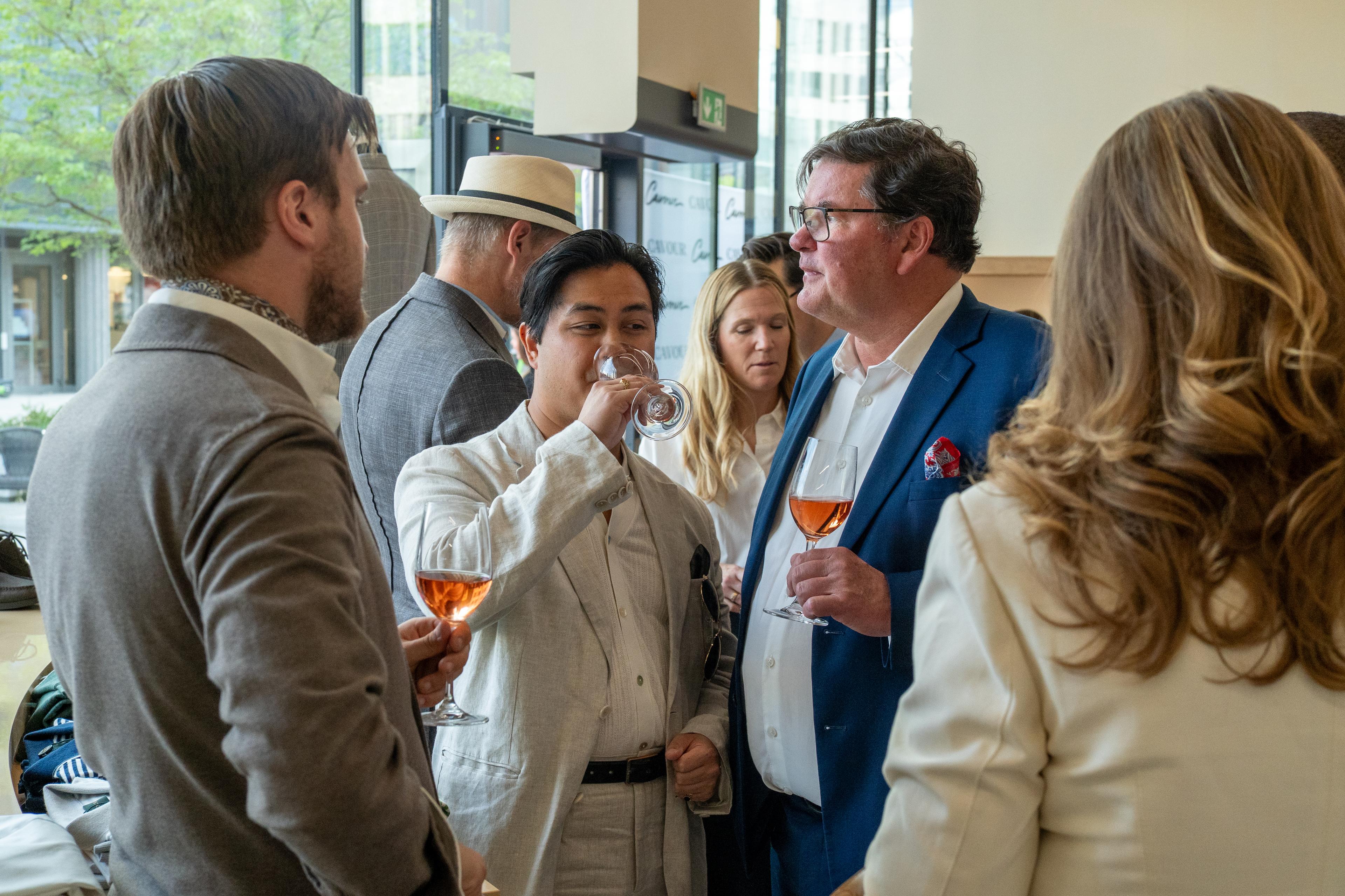 a group of people are standing around talking and drinking wine .