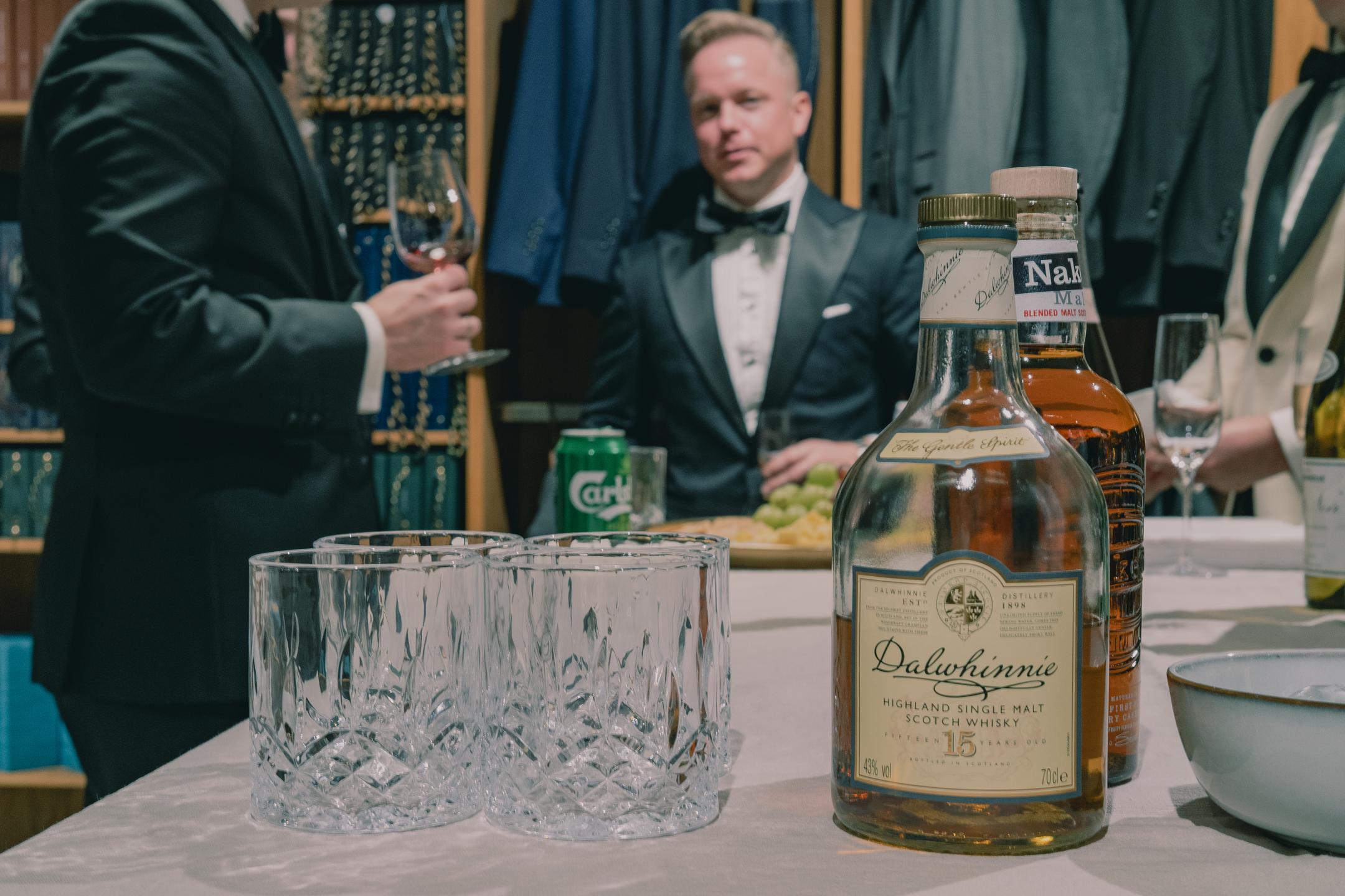 A table with whiskey on it and men wearing tuxedos in the background