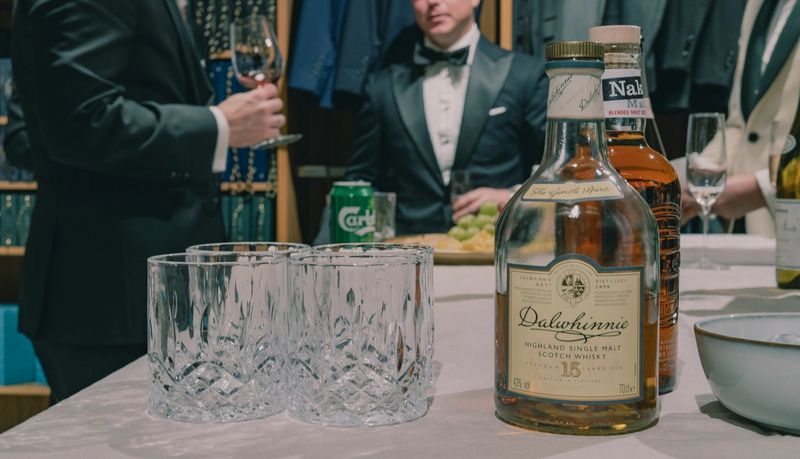 A table with whiskey on it and men wearing tuxedos in the background