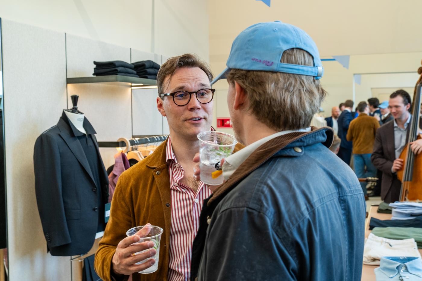 two men are talking to each other in a store while holding drinks .