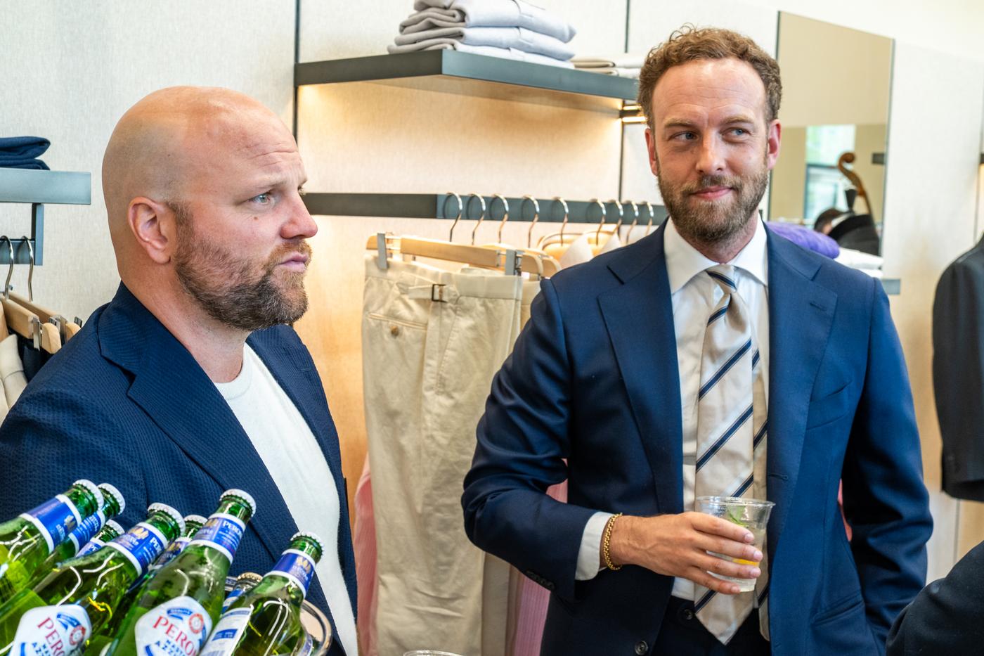 two men in suits and ties are standing next to each other in a clothing store .