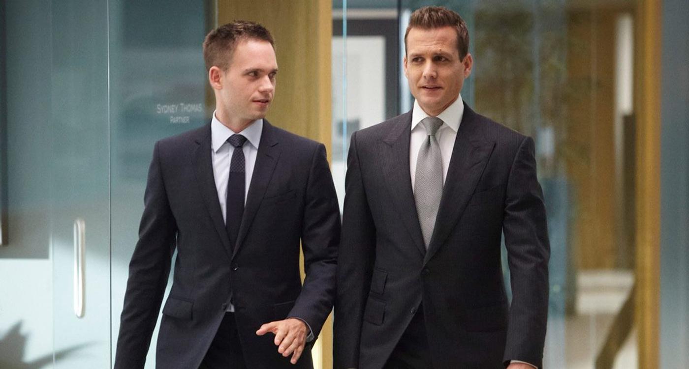 Mike Ross and Harvey Specter in suits walking through a modern office.