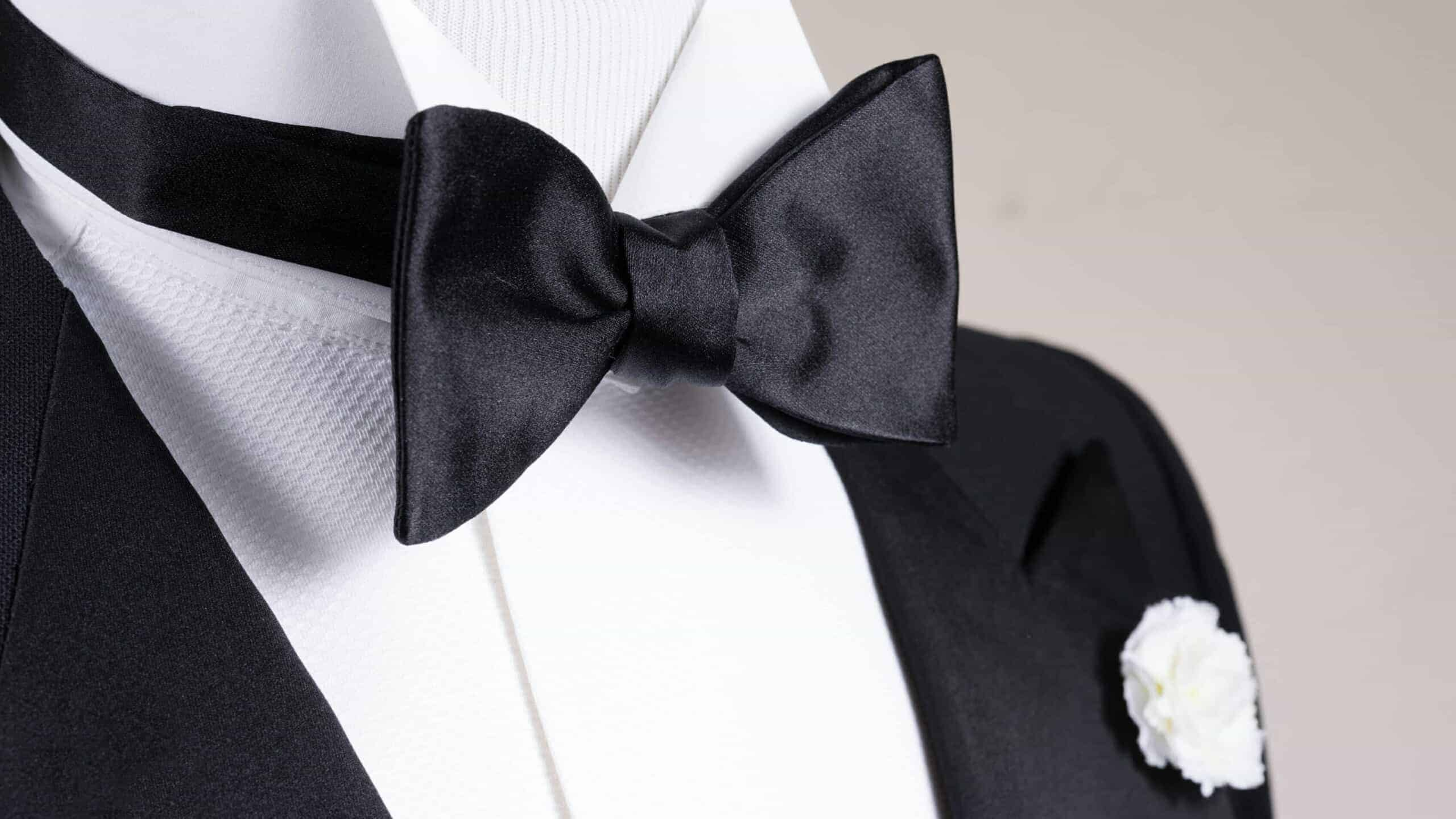 Black bowtie on a tuxedo outfit with a white shirt and lapel flower