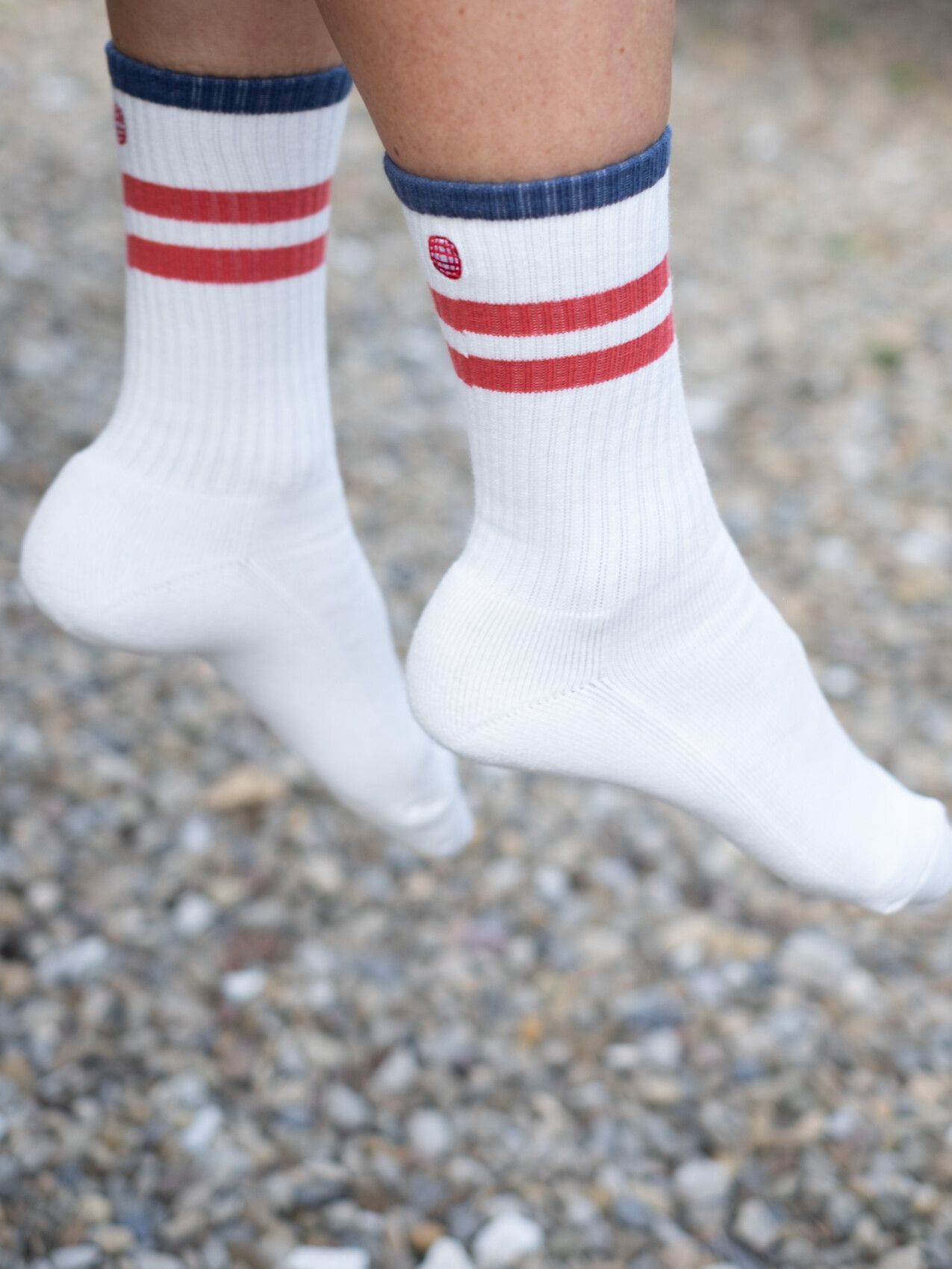 A person's feet dangle, wearing white socks with red stripes, blue cuffs, and a small red oval logo on the side.