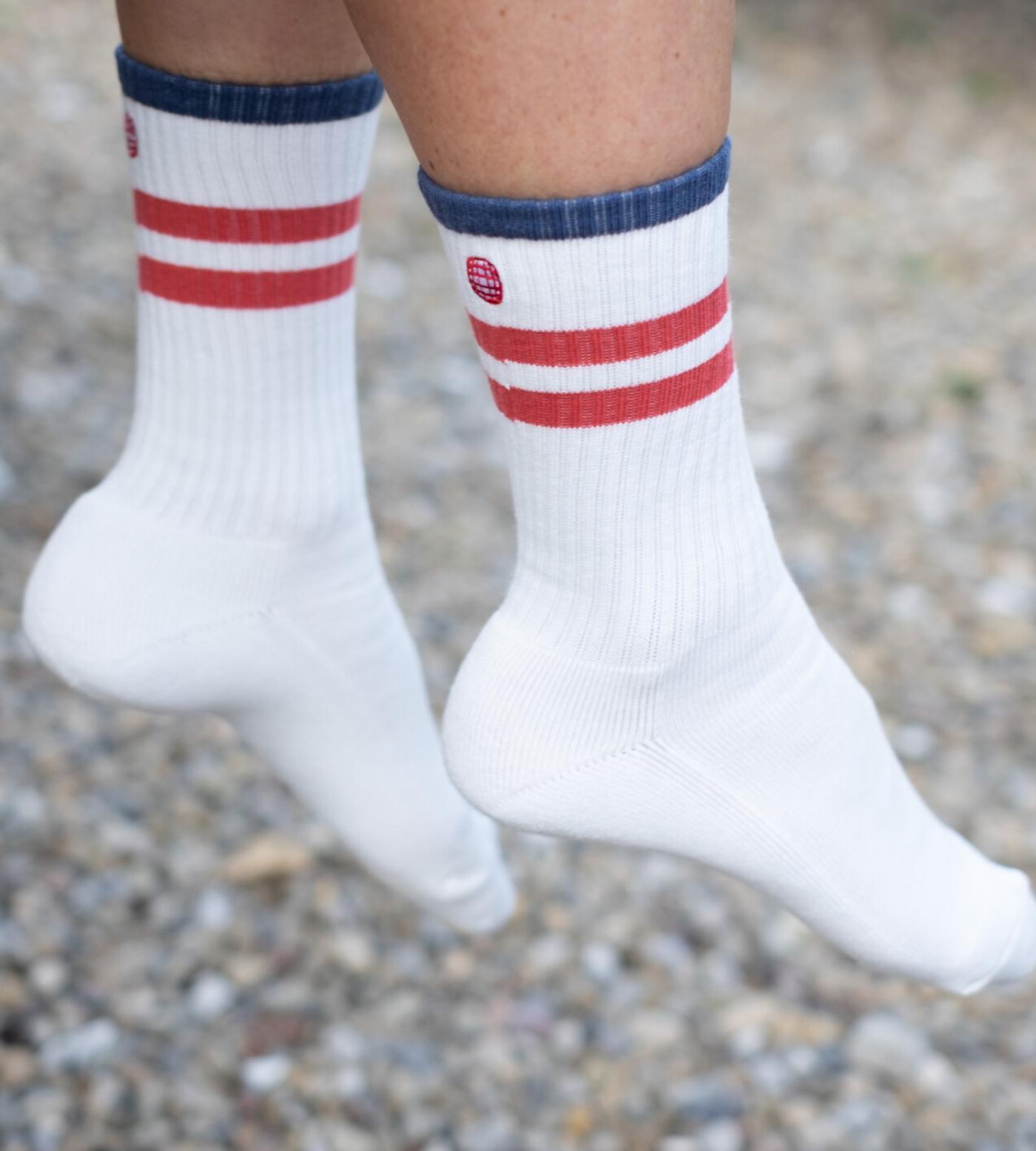 A person's feet dangle, wearing white socks with red stripes, blue cuffs, and a small red oval logo on the side.