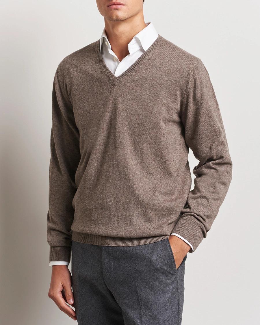 Man wearing a brown V-neck sweater over a white shirt and grey pants.