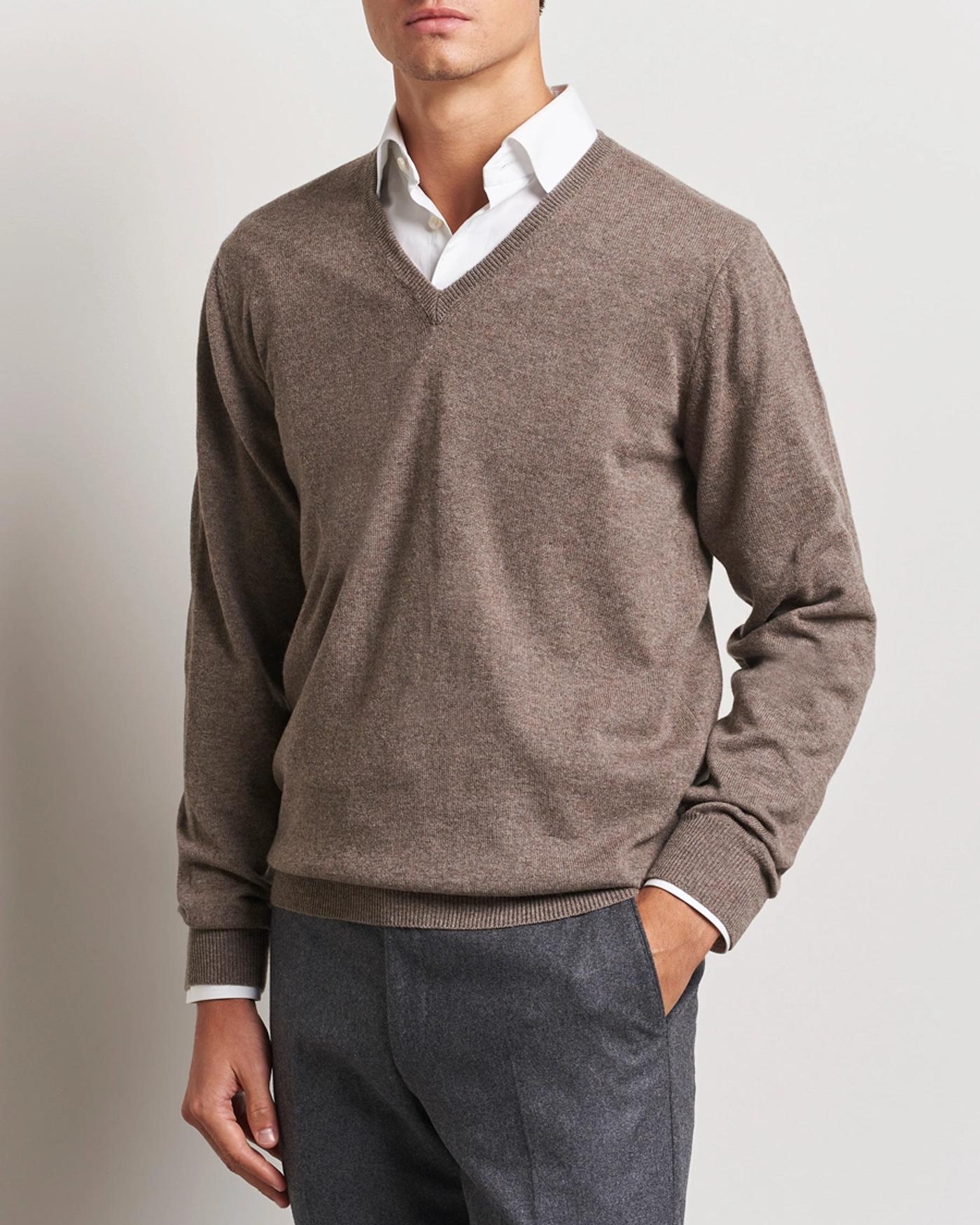 Man wearing a brown V-neck sweater over a white shirt and grey pants.