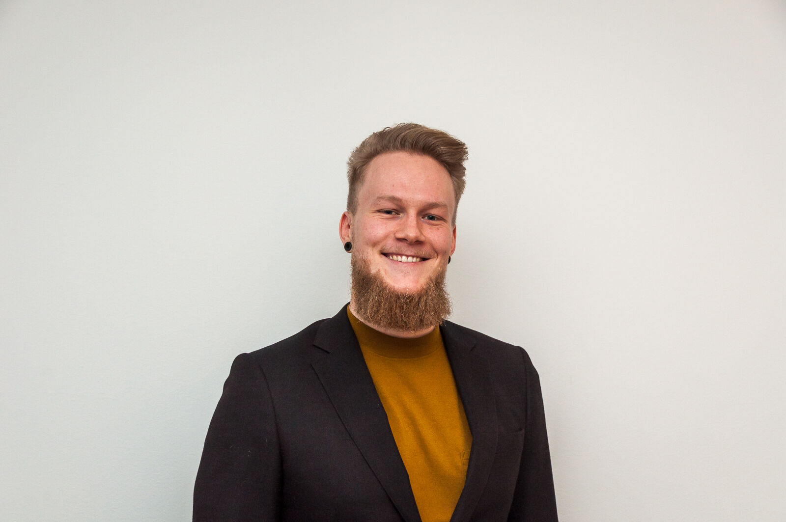 a man with a beard is wearing a brown suit and a yellow sweater