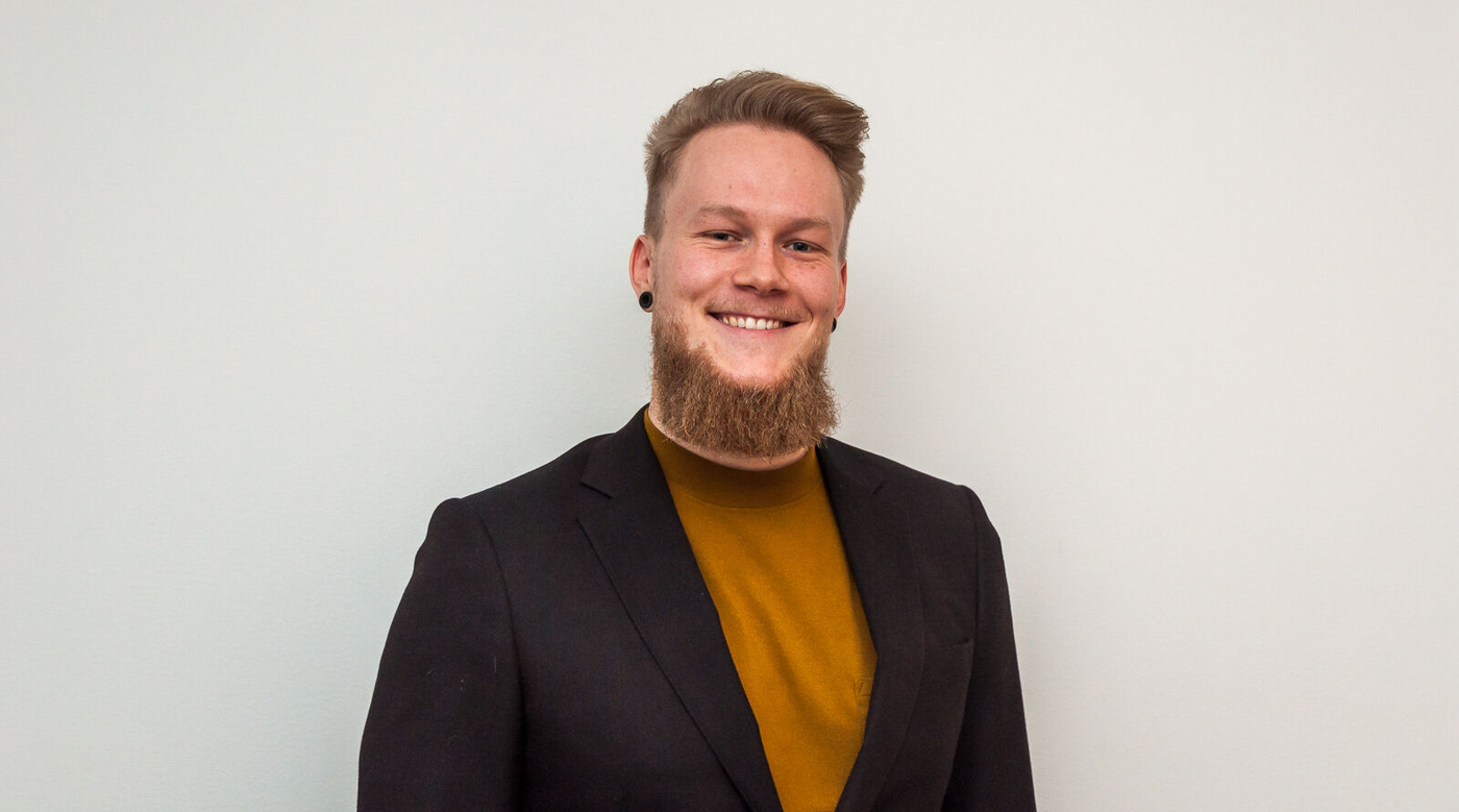 a man with a beard is wearing a brown suit and a yellow sweater