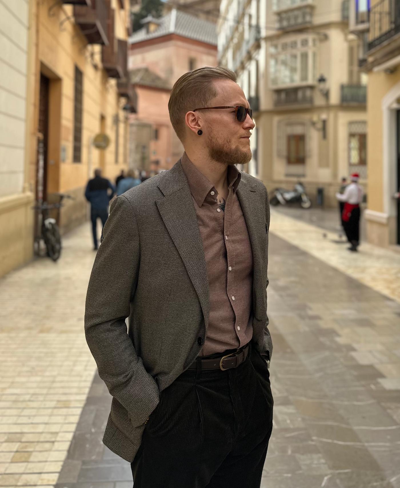 a man in a suit and sunglasses stands on a city street