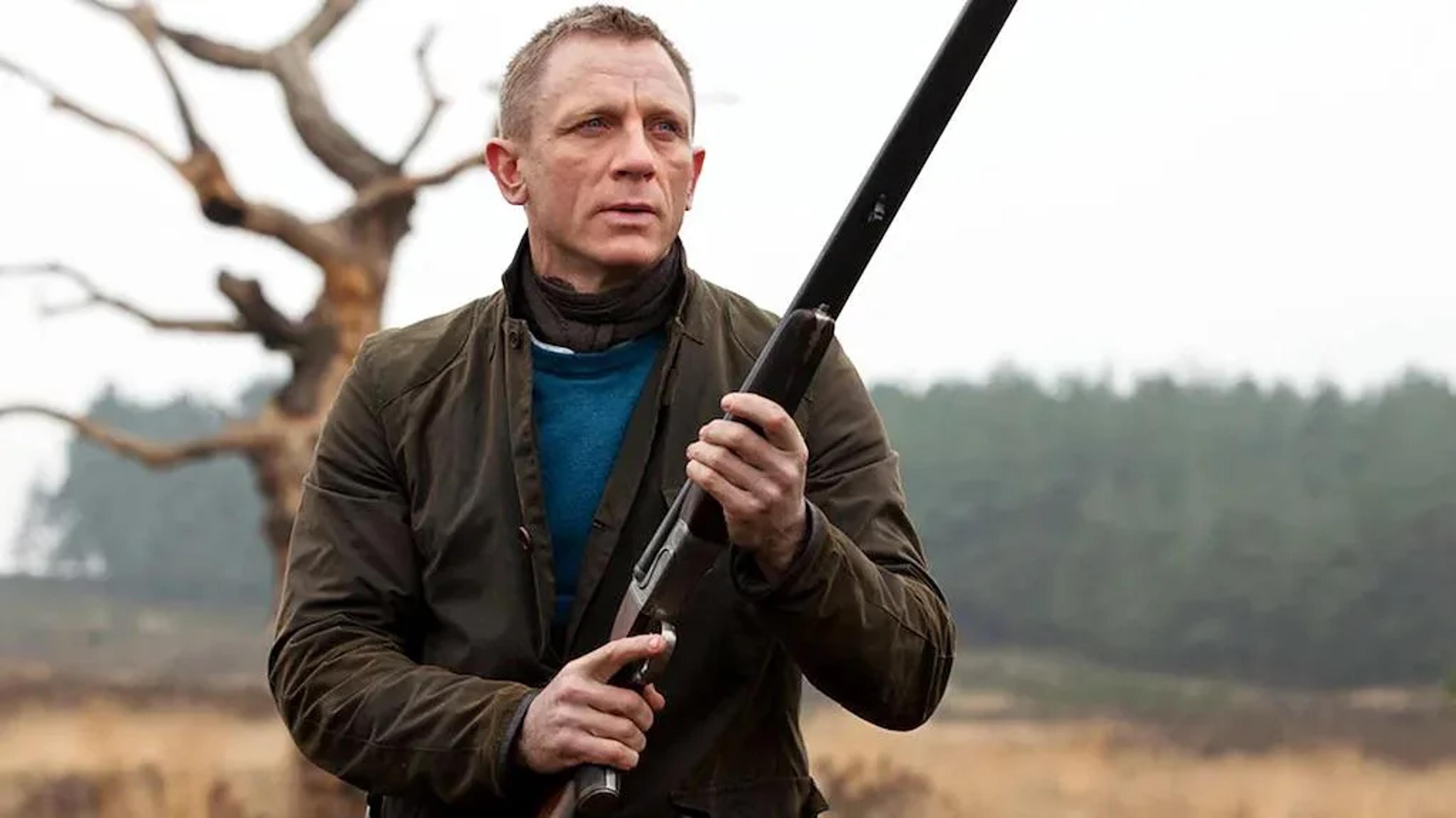Daniel Craig holding a shotgun in a rural landscape.