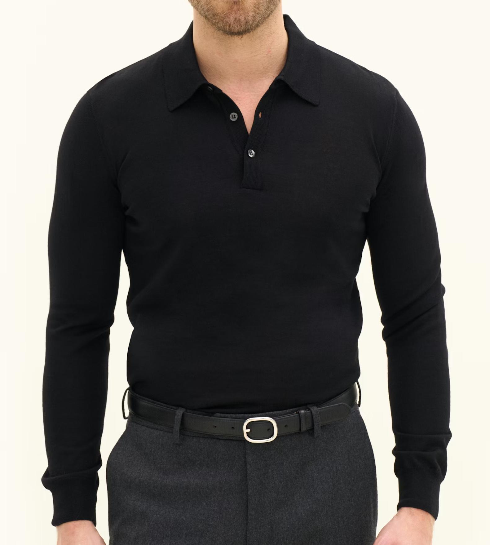A man wearing a black long-sleeved knit polo shirt, dark gray trousers, and a black belt stands against a light background.
