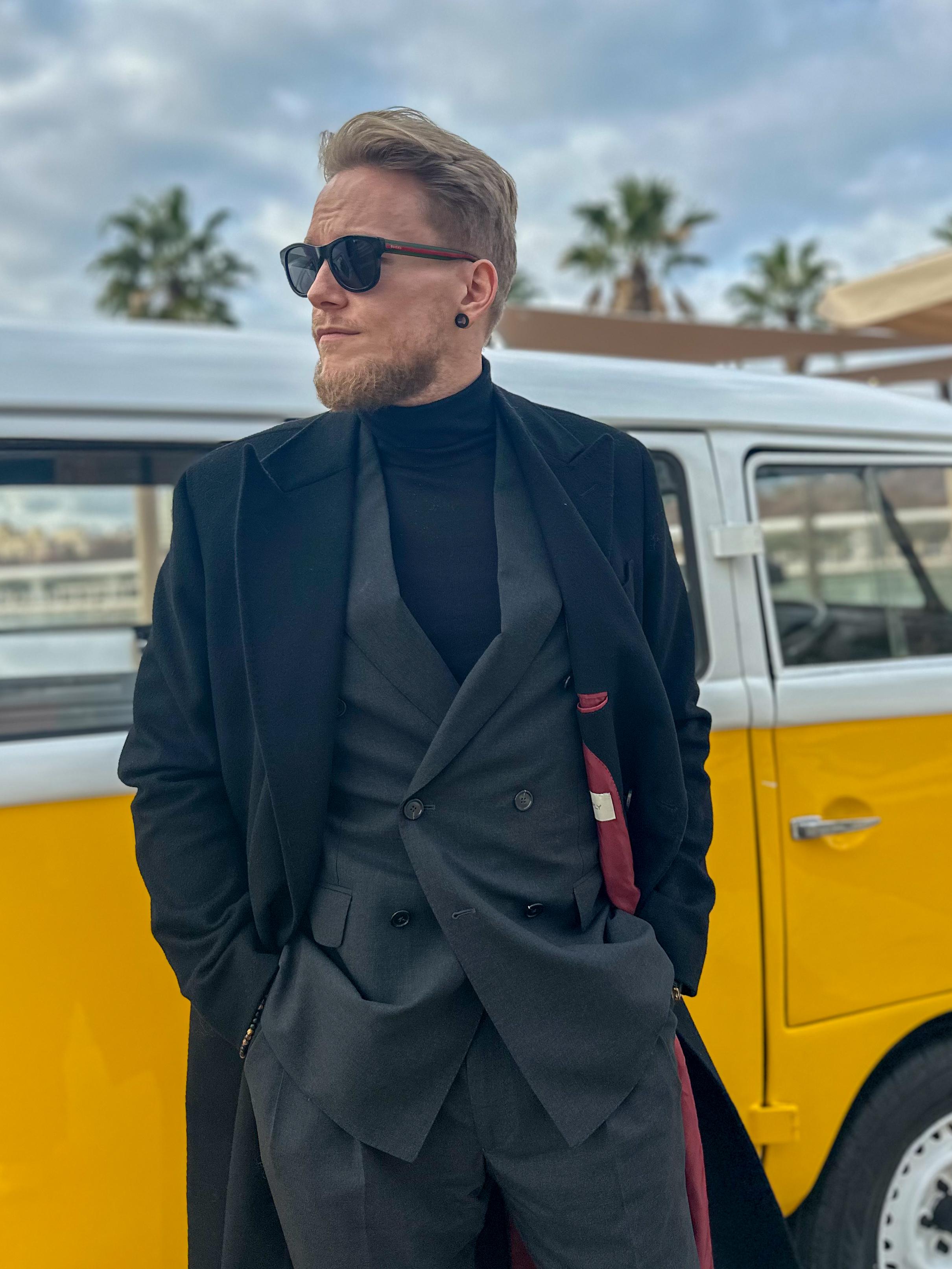 a man in a suit and sunglasses is standing in front of a yellow van .