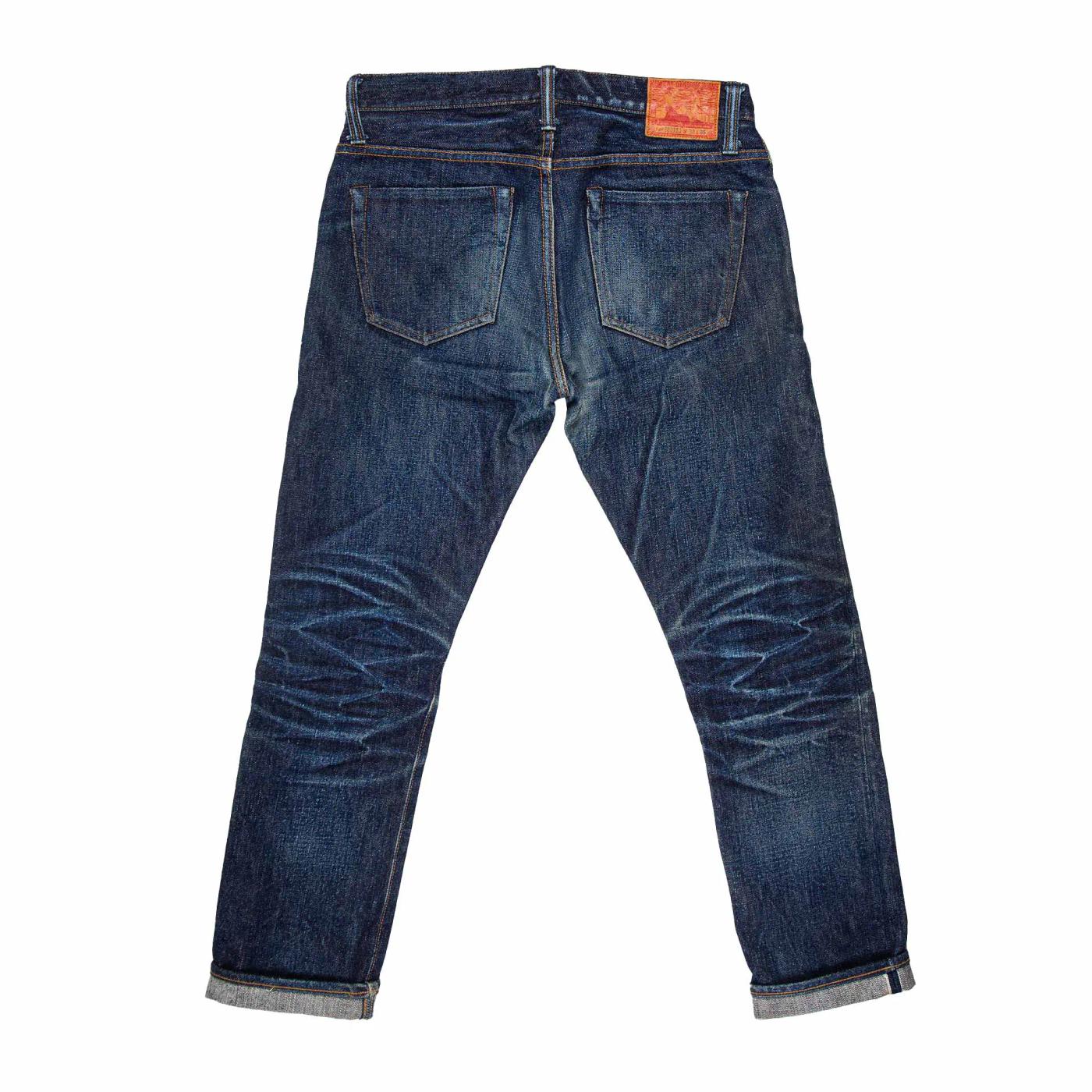 Back view of dark blue jeans with prominent fading, creasing, a red leather patch, and cuffed hems.