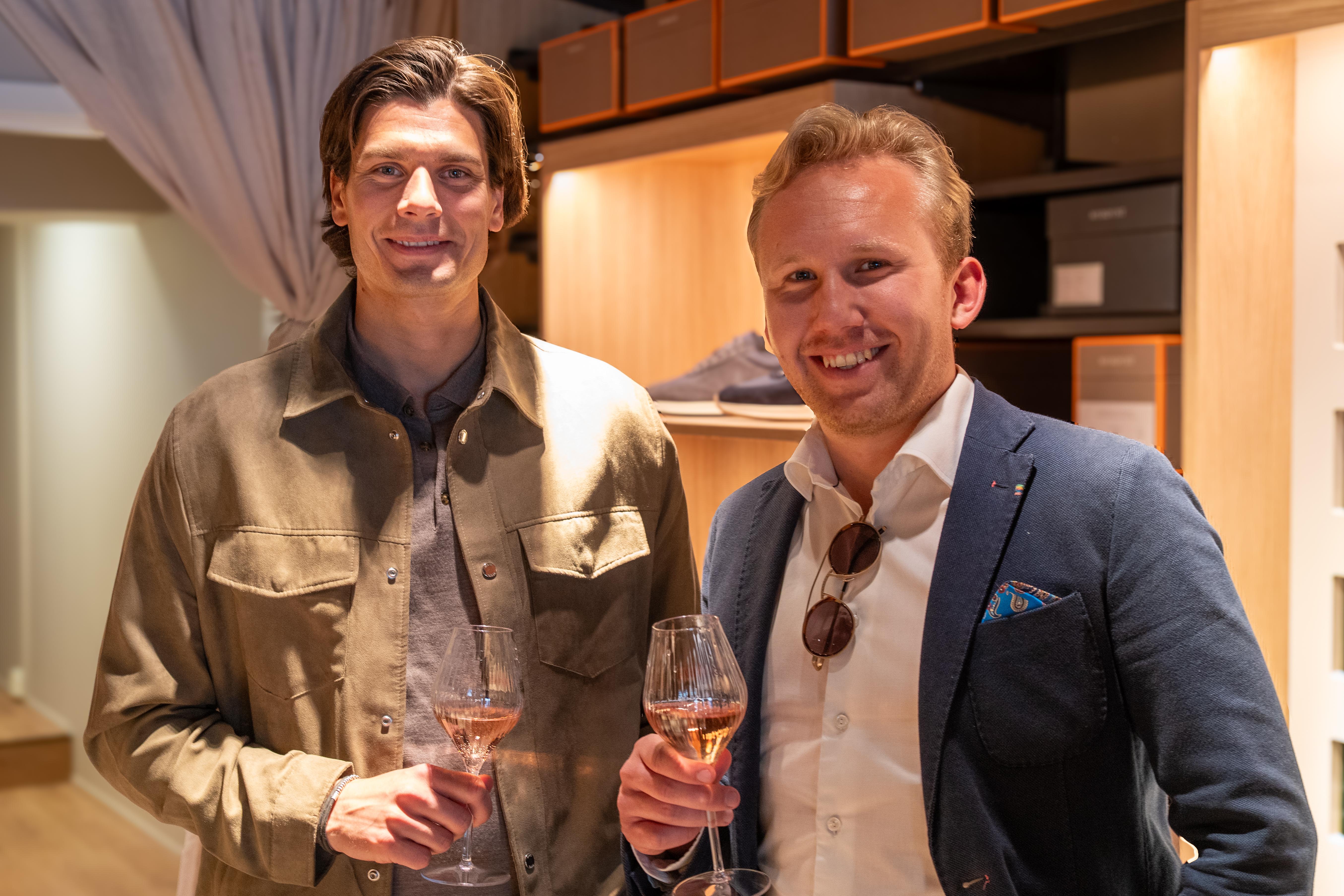 two men are standing next to each other holding wine glasses .