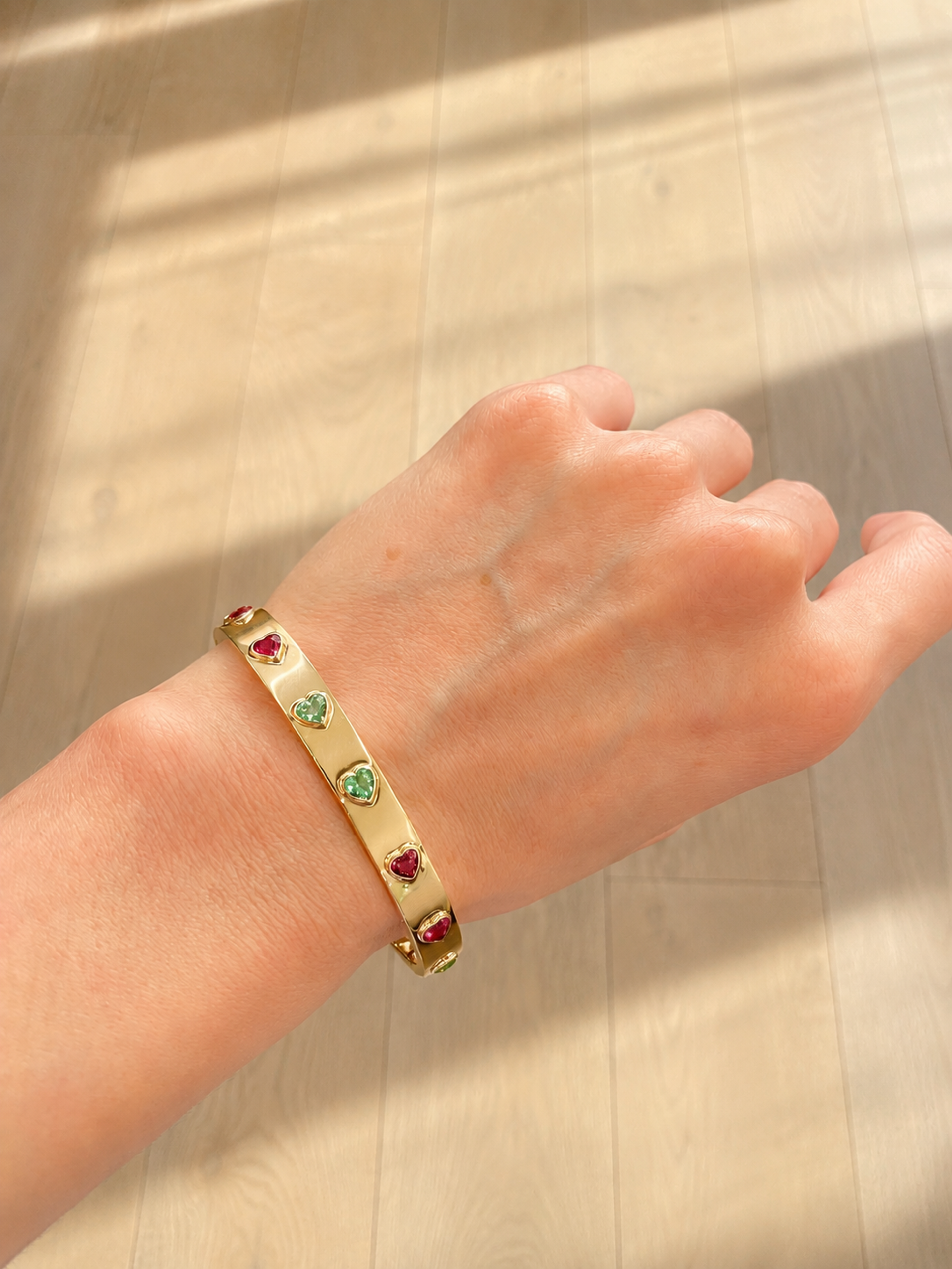 Rose gold bangle, heart-cut gemstones, worn on wrist