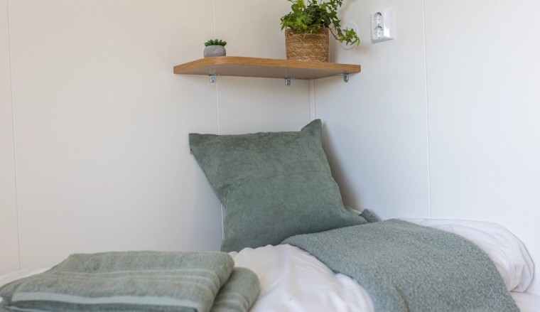 Bed with soft linens, towels, and a shelf with plants for a cozy touch.