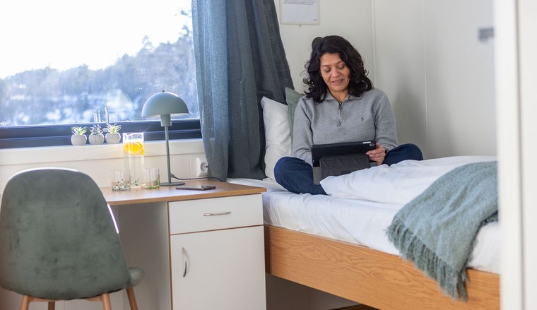 Woman relaxing in her room, sitting on the bed with a tablet.