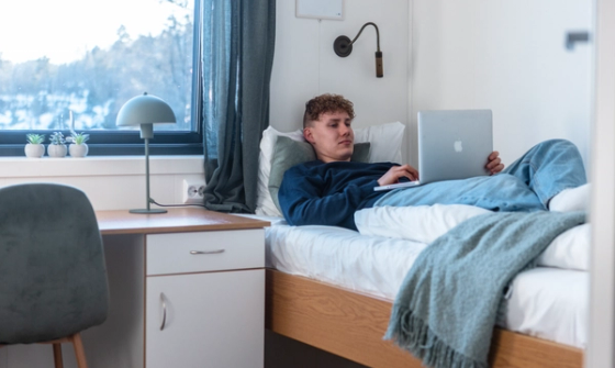 Person som ligger på en seng på et enkeltrom og ser på pc
