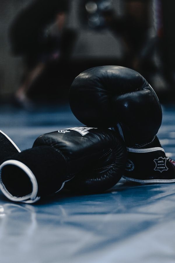 A pair of black boxing gloves rests on a blue mat.