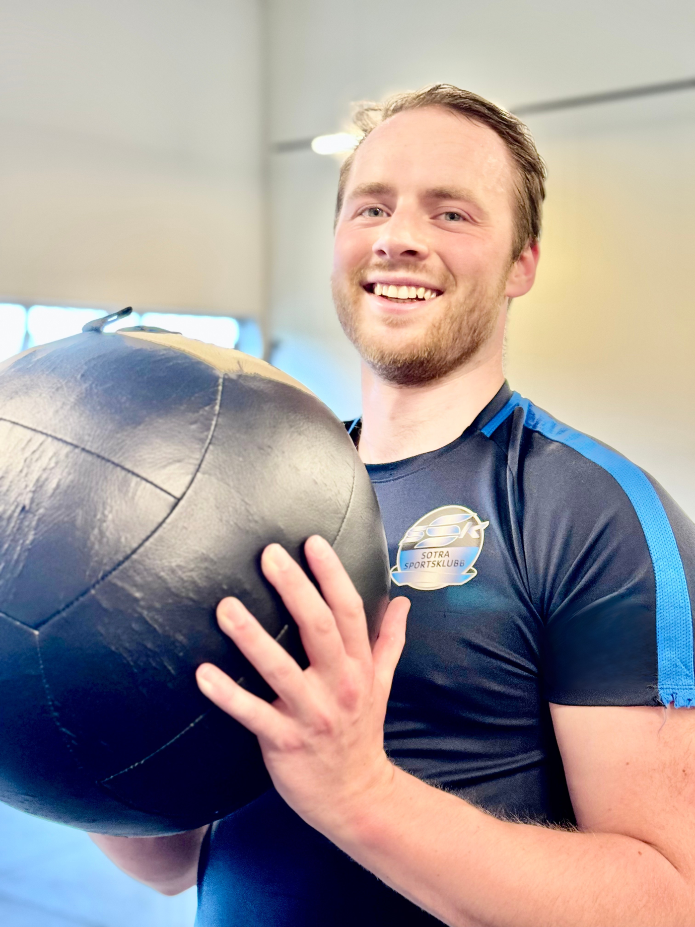 Smiling man holding a black medicine ball.