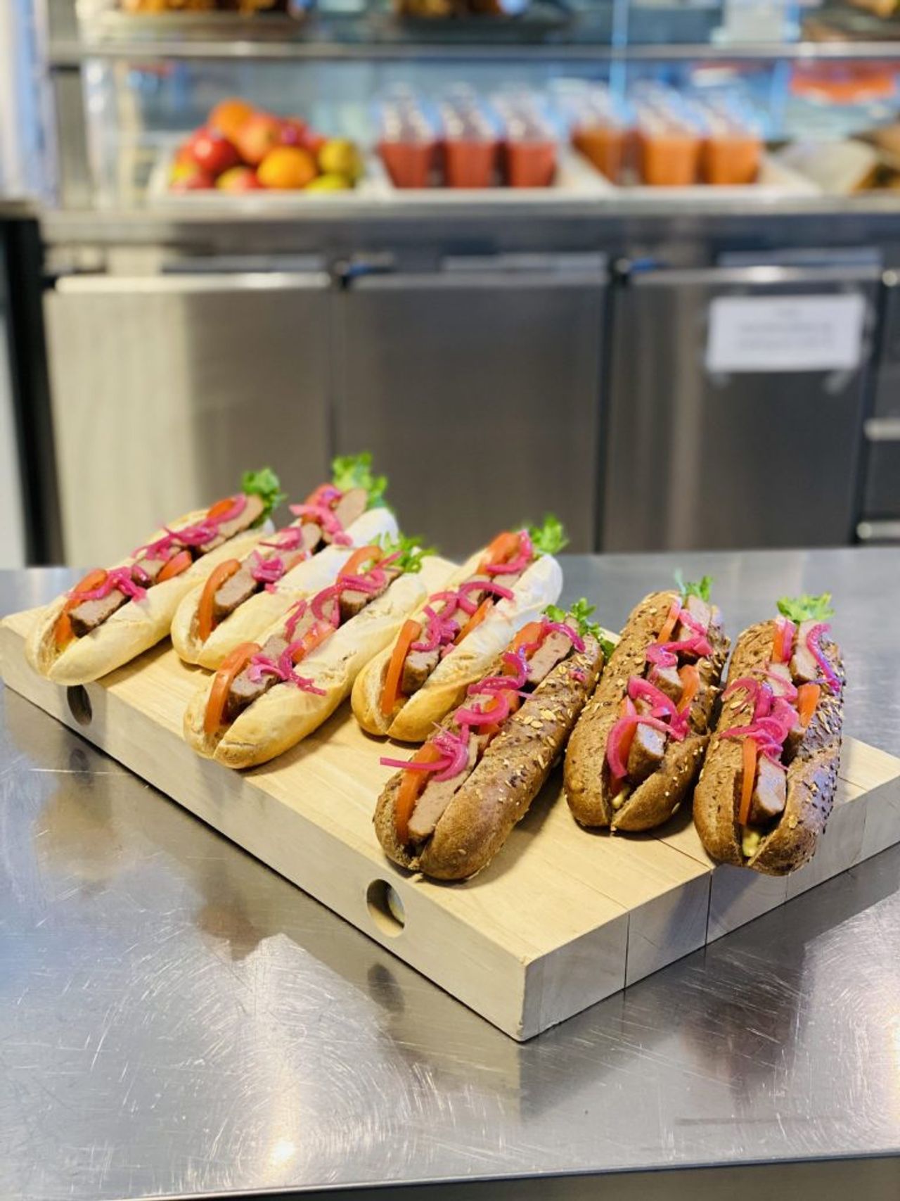 Hot dogs in buns topped with lettuce, tomato, and red pickled onions on a wooden board.