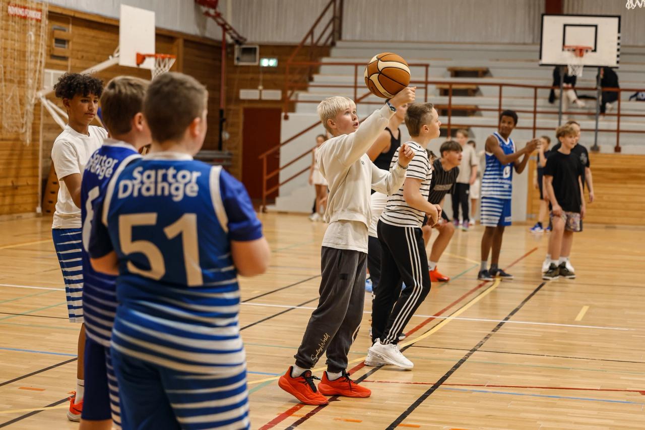 A group of boys playing basketball in a gym, with one boy holding a basketball up.