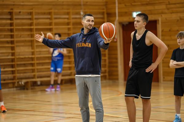 A basketball coach holds a ball and instructs young players in a gym.