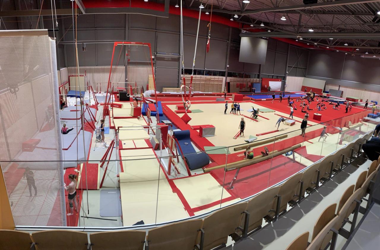 Gymnastics gym with many people training on red mats, balance beams, and bars.