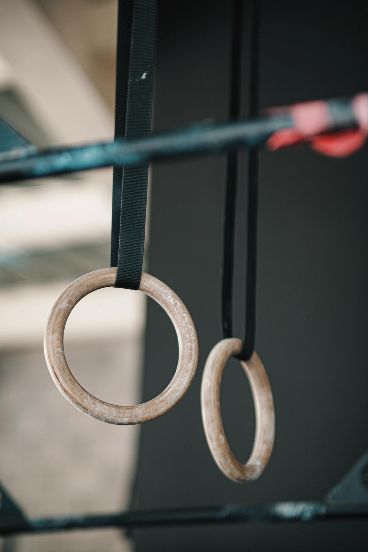 Two wooden gymnastics rings hang from black straps.