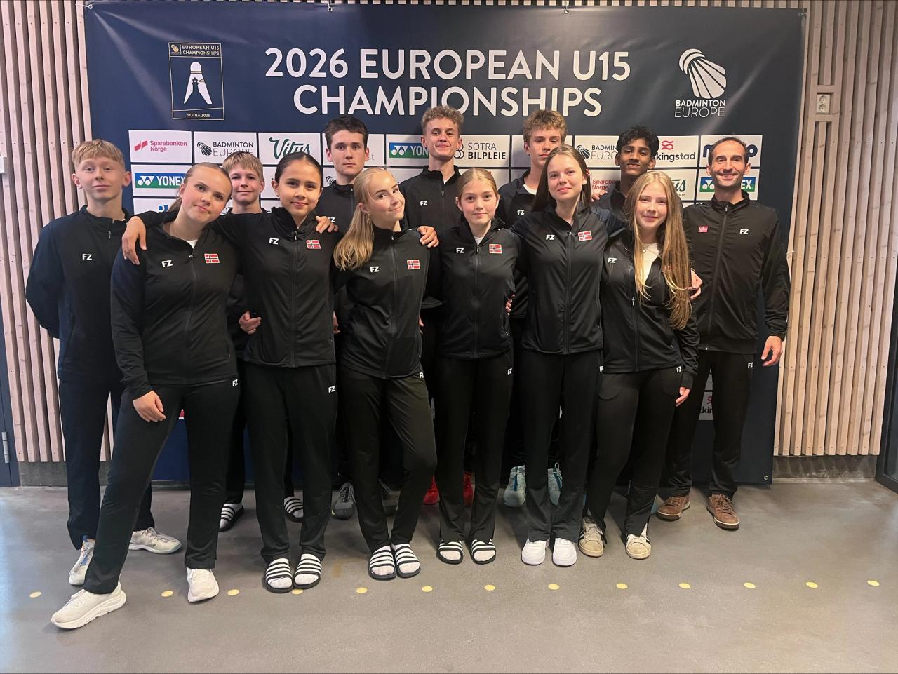 A group of young athletes and two adults in black tracksuits stand in front of a "2026 European U15 Championships" banner.